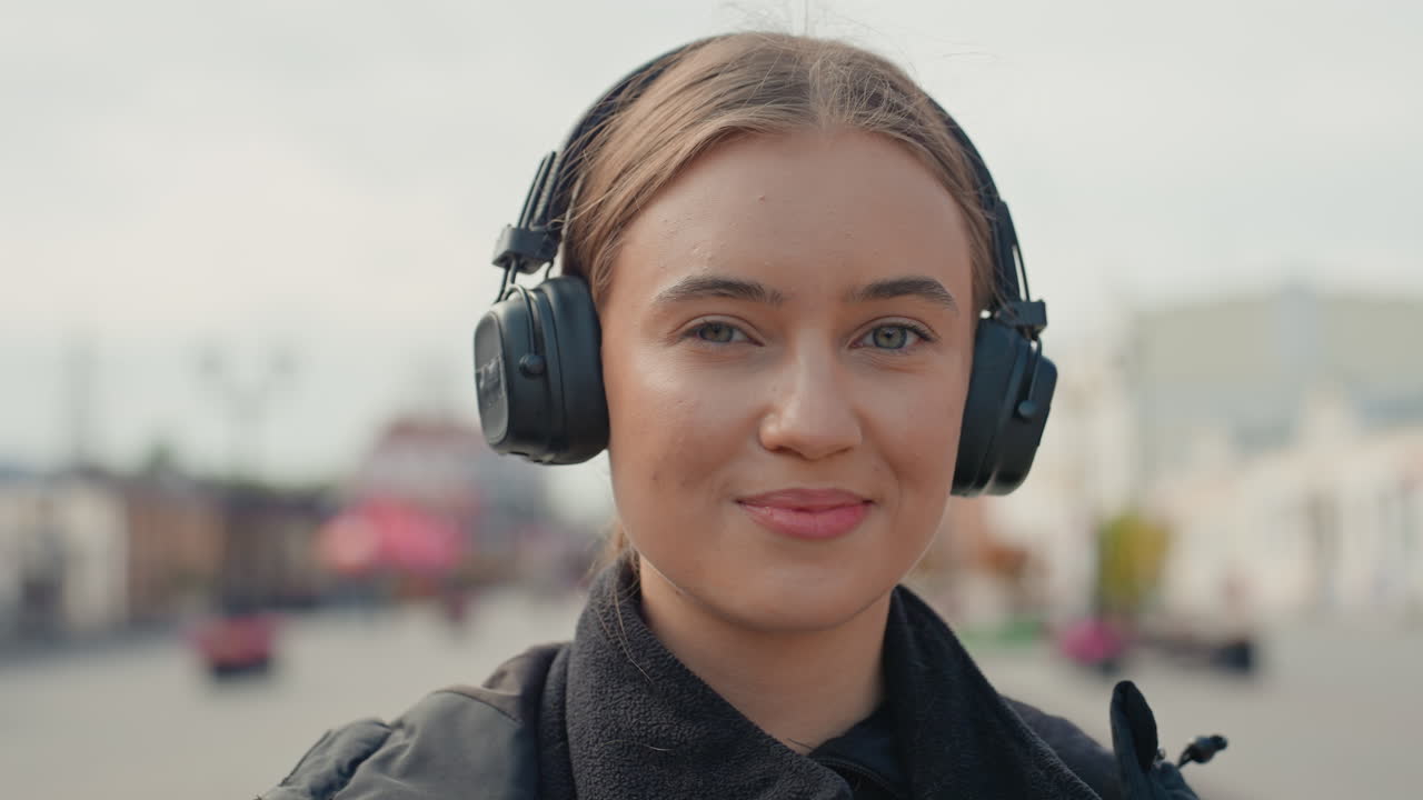 Mujer caucásica con auriculares tomando café; una viajera que disfruta de su bebida matutina mientras camina por el paseo marítimo con luz tenue, poca profundidad de campo, retrato espontáneo, sonrisa discreta y ambiente acogedor.