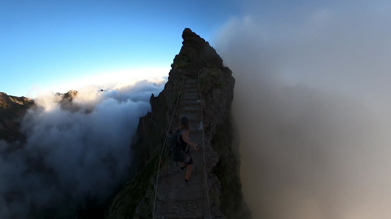 360 wide POV shot of a young, fit and athletic man hiking up to the top of Pico das Torres in Madeira. Steep edges on both sides as he walks up the steps of the ridge during beautiful sunrise.