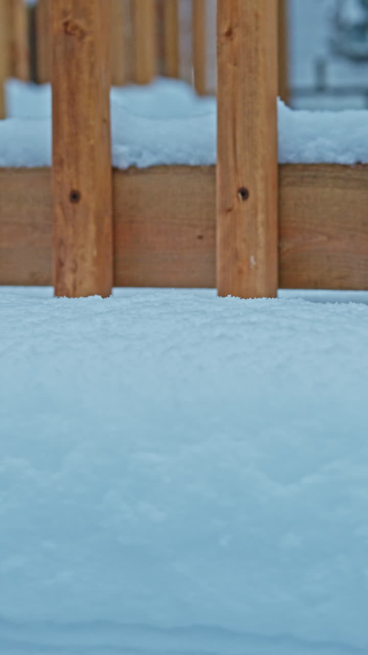Ensimmäinen lumi peittää puisen terassin pohjaa asuintalon takapihalla, mikä merkitsee vuodenaikojen vaihtumista syksystä alkutalveen.