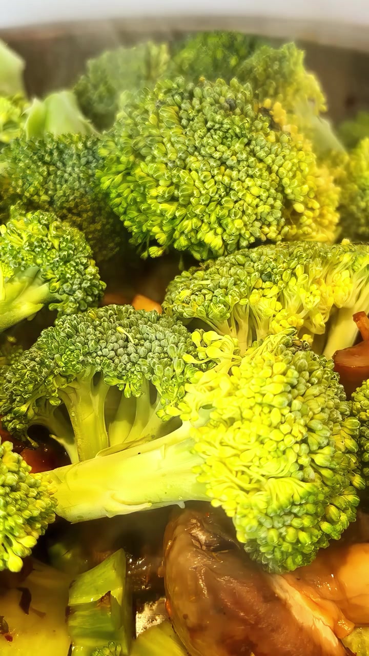 Cimette di broccoli freschi e verdi e altre verdure che cuociono a vapore in una pentola calda, vista ravvicinata.
