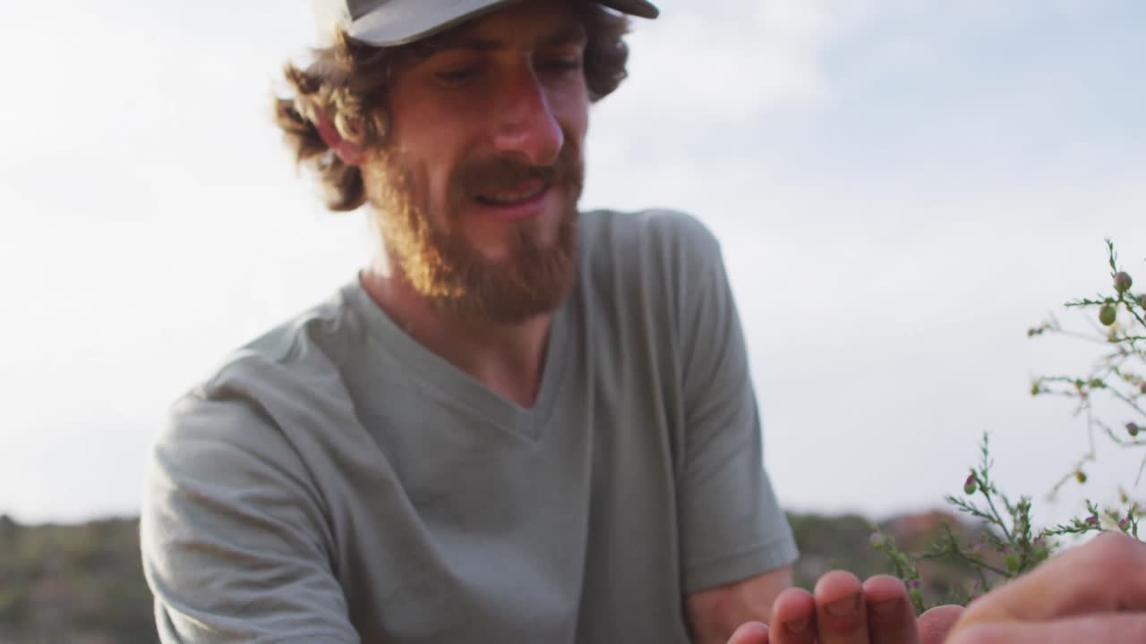 feliz barbudo caucásico hombre sobreviviente recogiendo bayas y sonriendo en el desierto