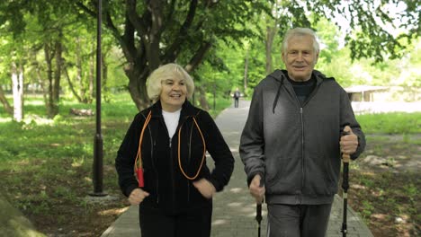 Active-senior-old-couple.-Man-training-Nordic-walking,-woman-running-in-park