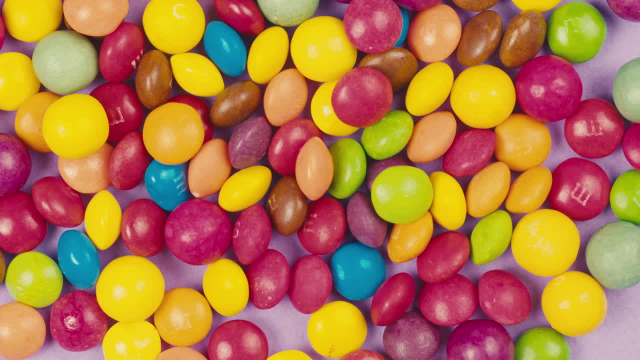 Colorful dragee candies on purple background. Summer bright texture studio shot for store, supermarket, close up top view. Children sweets made of sugar, mix of lollipops. beautiful bonbons.
