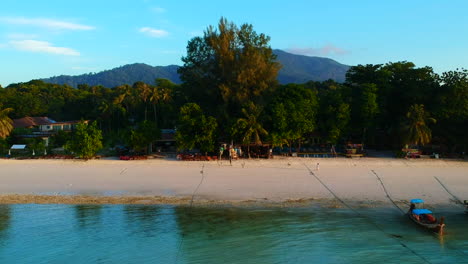 Aerial-shot-of-a-beach-with-white-sand,-boat-being-park,-an-ocean-and-green-trees-in-the-background