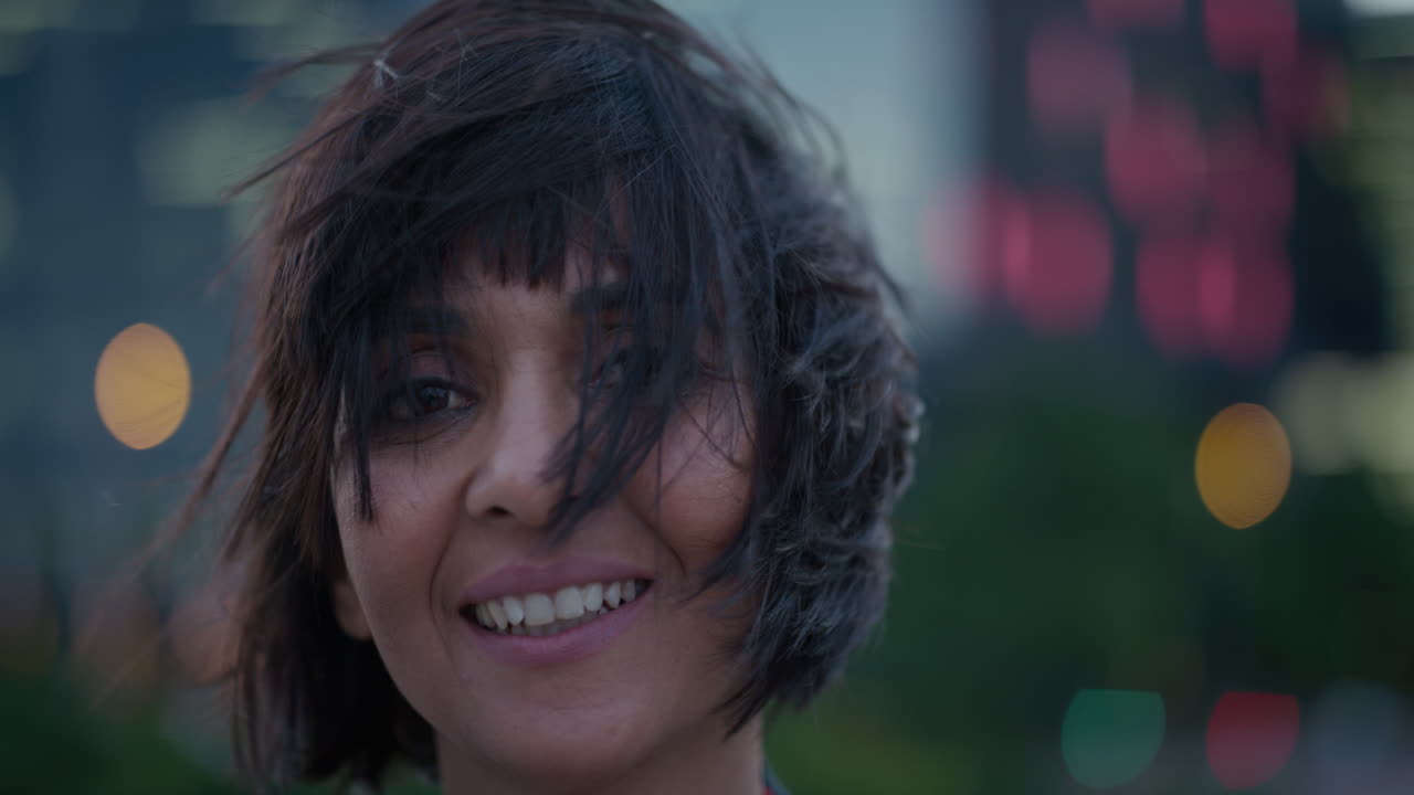 retrato de cerca hermosa mujer hispana gira la cabeza sonriendo disfrutando de la ciudad relajada noche viento soplando el cabello exitosa mujer étnica mirando feliz cámara lenta