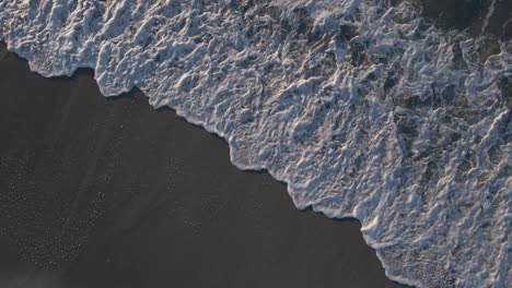 majestic ocean waves rolling over sandy beach leaving foamy trace, aerial top down shot