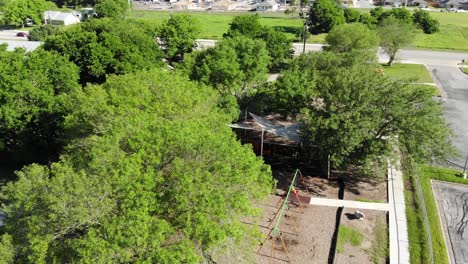 Flying-straight-back-across-the-tops-of-the-trees-that-shade-the-playground,-large-swing-set-and-playground-equipment-come-into-view