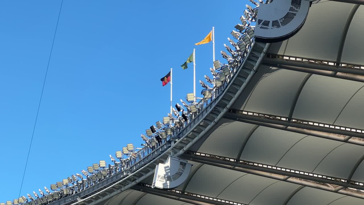 Flags flying atop Optus Stadium Perth lights canopy low side angle