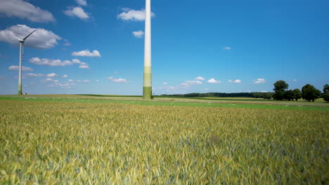 aerial backwards flight over agricultural wheat field with rotating wind mill against blue sky in background