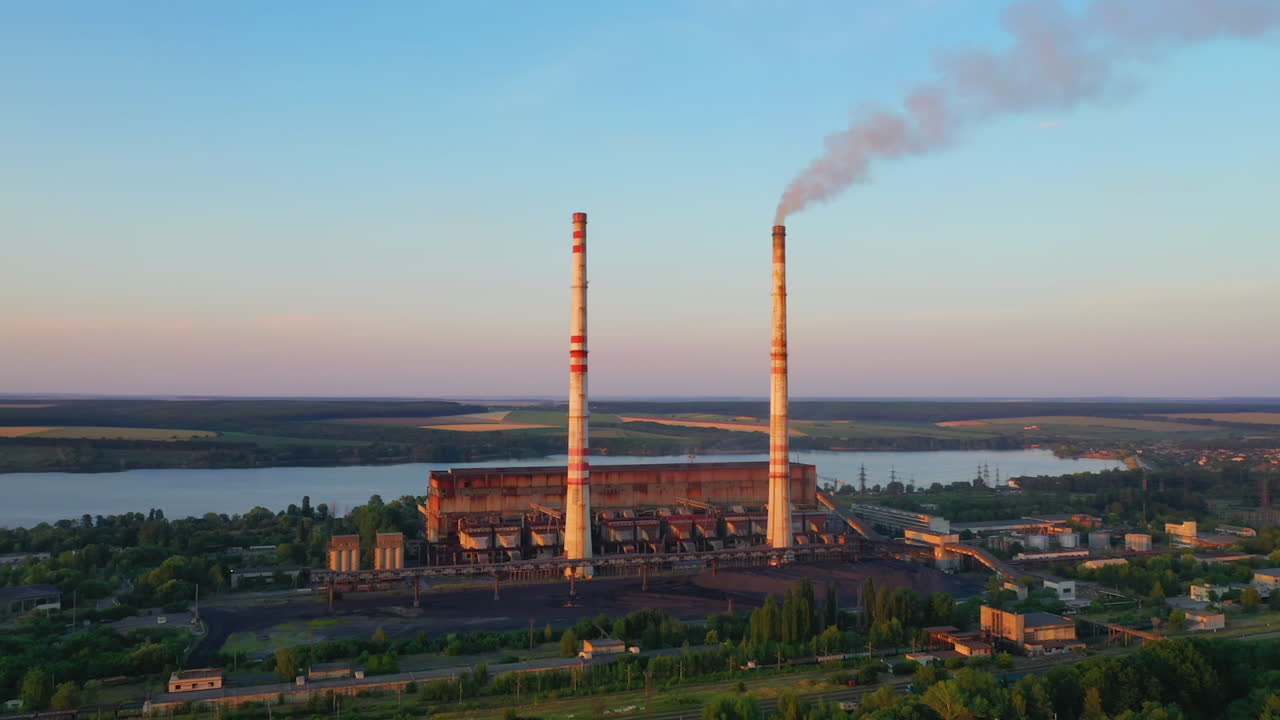 Industrial zone with chimneys at sunset. Panoramic view on pipes with smoke of factory on nature background. Environmental pollution.