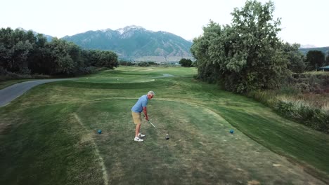 drone shot fly-over over a golfer on a tee box who swings and drives his golf ball into the fairway