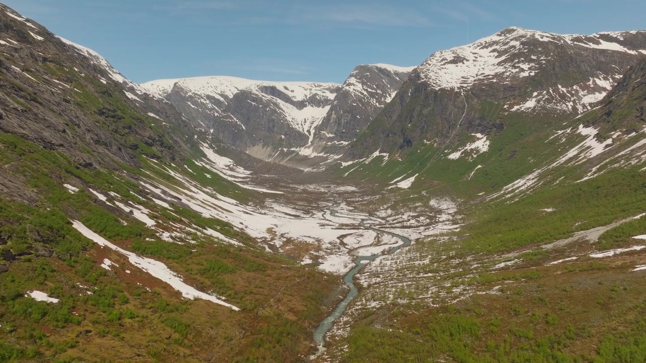 Video cinematografico con drone attraverso la valle di Austerdalsbreen, che rivela un fiume glaciale turchese e tortuoso, montagne innevate e un ghiacciaio sotto un cielo estivo limpido e azzurro. Paesaggio selvaggio epico della Norvegia.