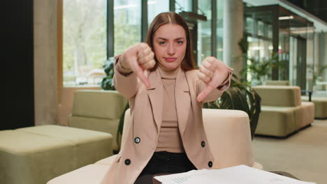 portrait of upset caucasian businesswoman sitting in office lobby showing thumb down sign gesture