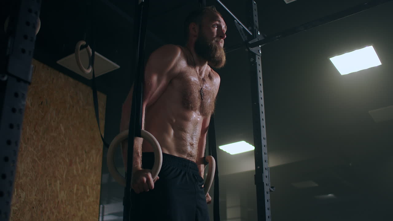 Strong bearded male athlete performs push-ups on gym rings in slow motion in the gym