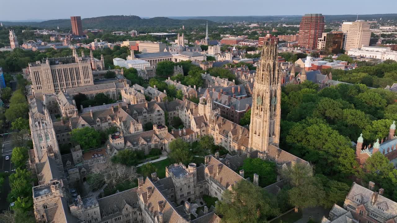 Old campus courtyard with harkness tower in New Haven, Connecticut. Aerial top down rising shot. Sunset time in well-kept park of high school university. Ancient buildings and houses in town