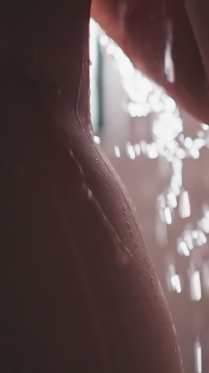 Bare woman with falling down water sprays in bathroom closeup. Skinny lady stands under pure shower jets in washroom. Relaxation and body washing