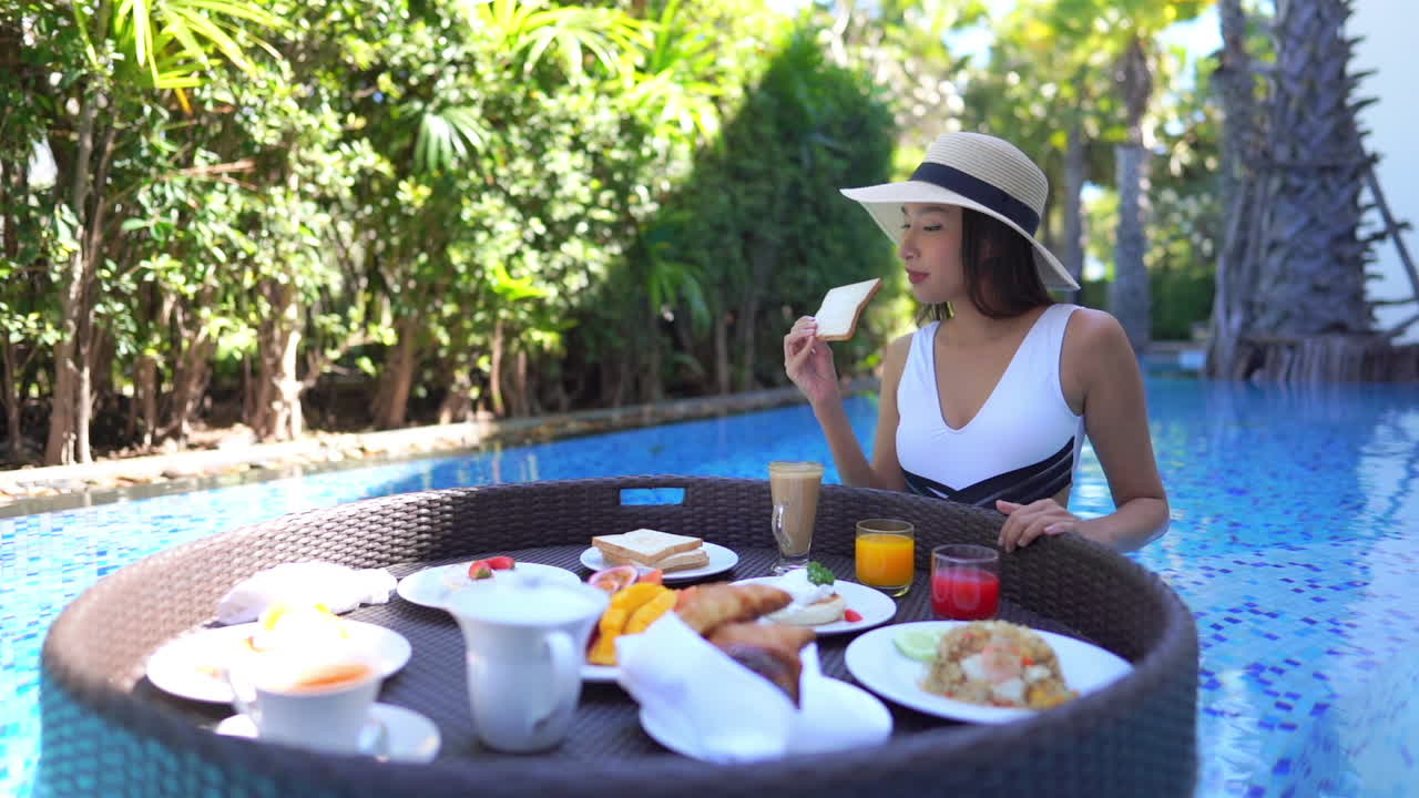 A lovely young Asian woman spins a floating platter of breakfast food picking up a piece of toast to eat