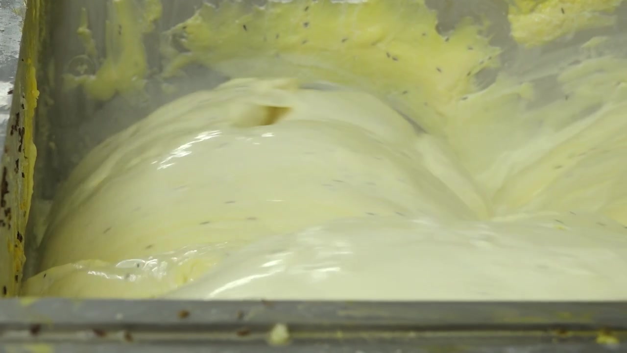 Tyk gul osteblanding, der behandles i en industriel ostefabriksmaskine, og viser glat mejeritekstur under produktionen.
