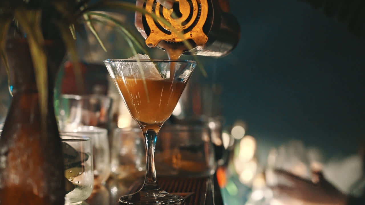 Barman che versa un cocktail in un bicchiere da Martini con ghiaccio.