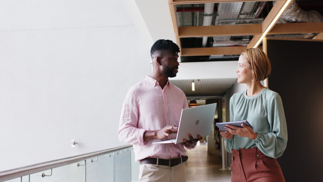 Discussing project details, colleagues using laptop and tablet in modern office