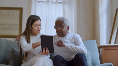 mujer joven ayudando a su abuelo con el uso de la tableta.