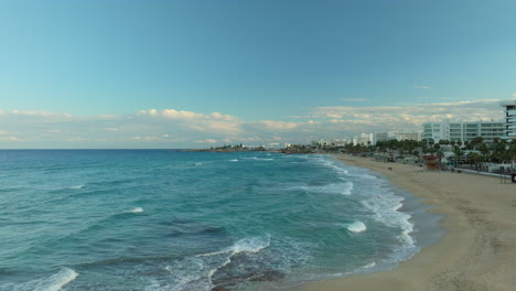 an aerial view of the coastline in protaras, cyprus, featuring the clear blue sea, gentle waves, sandy beaches, and a coastal town with modern buildings stretching along the shore