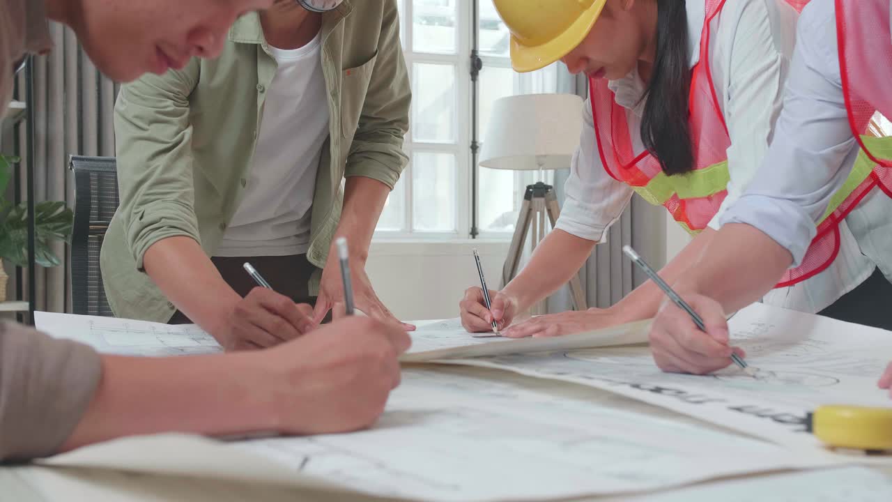 Three Asian Engineers With Helmets Helping A Man Drawing Building Construction At The Office