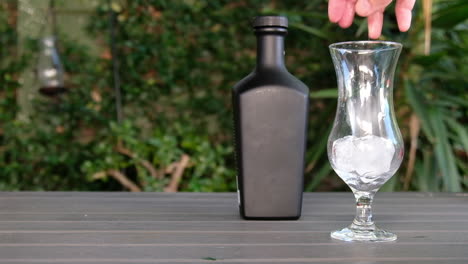 el hielo se cae en un vaso como parte de la elaboración de un gin-tonic en un jardín