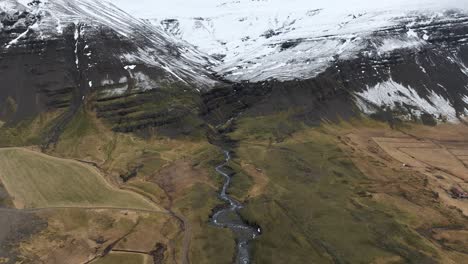 Río-Que-Fluye-Desde-Montañas-Nevadas-En-El-Hermoso-Paisaje-De-Islandia,-Aéreo