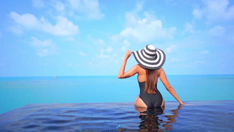 Back-of-woman-sitting-on-infinity-pool-border-with-stunning-view-of-tropical-sea-horizon,-static-full-frame