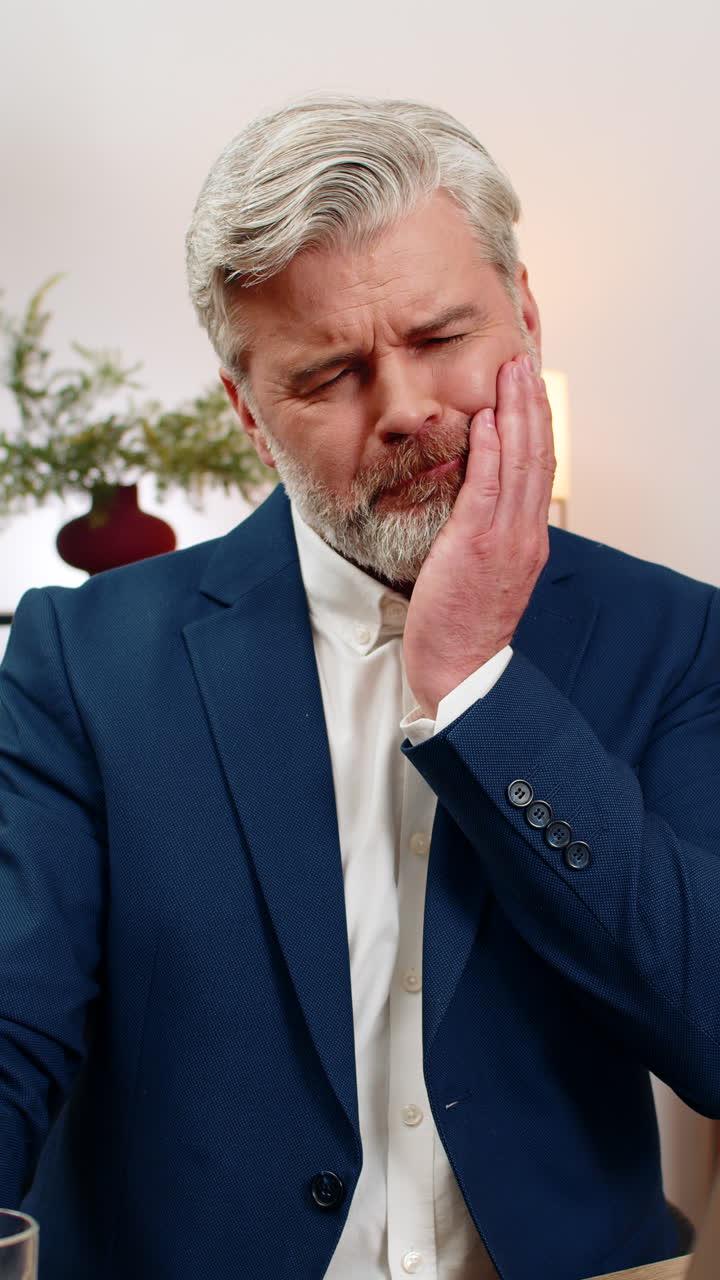 Middleaged businessman drinks cold water experiences tooth pain grips jaw grimacing seeking relief