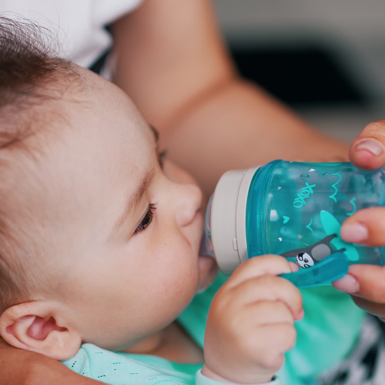 Baby drinking water from a plastic bottle with pacifier. Mommy holding a bottle for her son. Close up