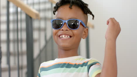 african american boy with a bright smile wears blue sunglasses and a striped shirt at home
