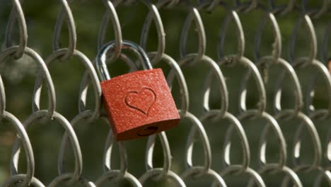 close-up of a hand placing a heart-engraved padlock on a chain-link fence