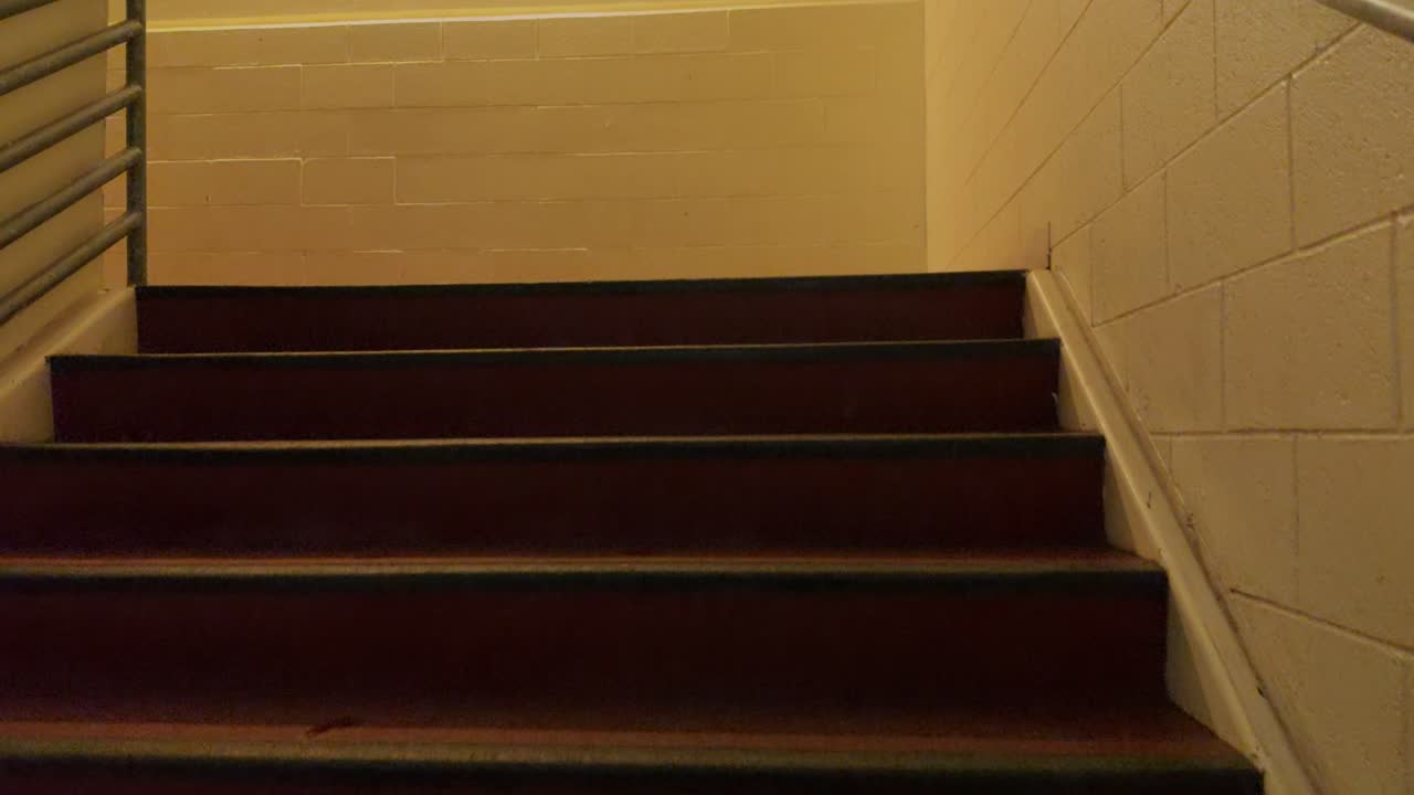 Handheld walk up and around an empty indoor stairwell with warm lighting and clean walls