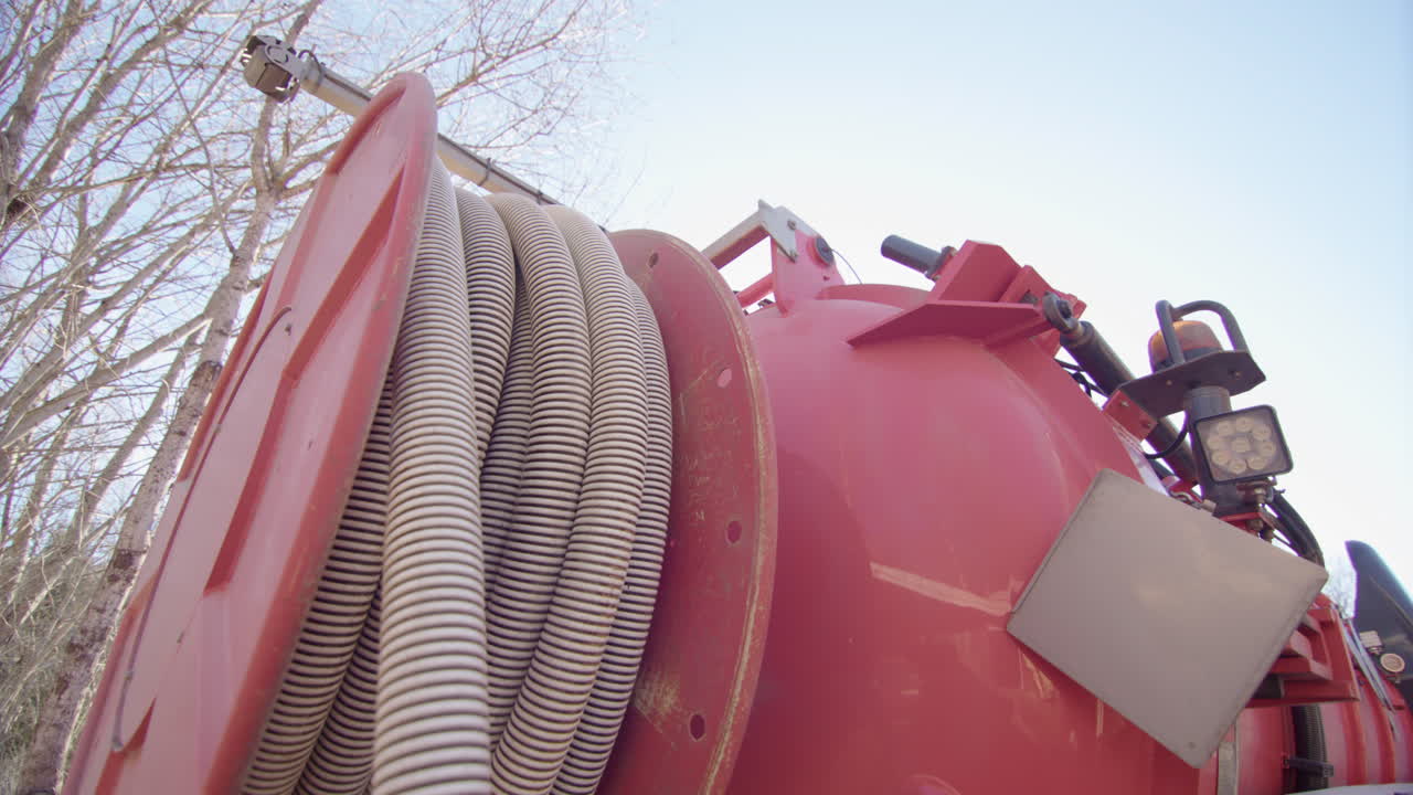 A vacuum truck winds its huge suction pipe back onto the reel, sunny