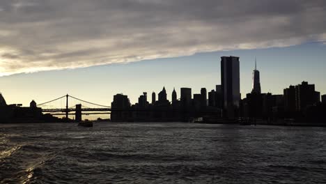 silhouette of new york city and bridge during sunset, view from hudson river