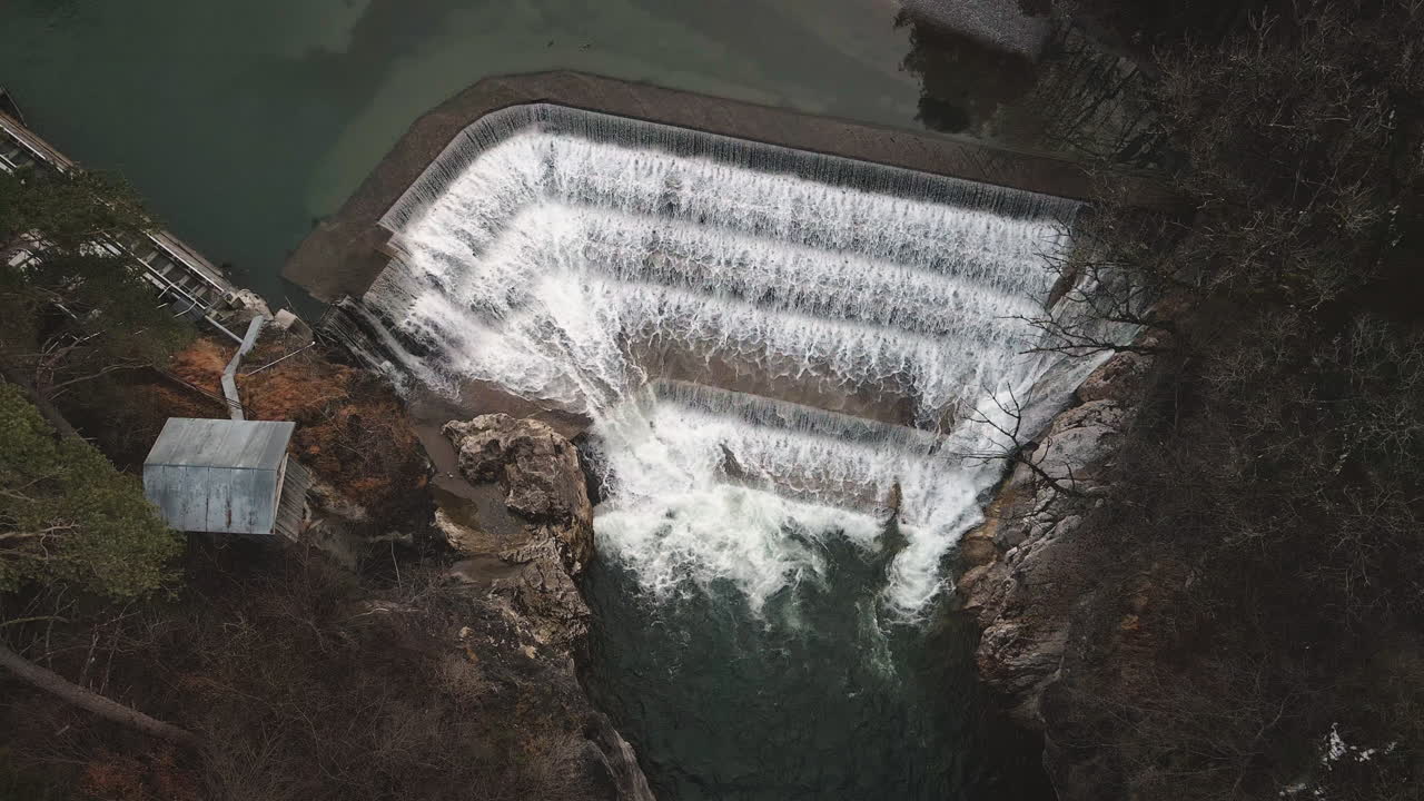 Drone i slowmotion daler ned til Lechfall-dæmningen i Füssen og fremhæver brusende hvidt vand, turkis reservoir og klippefyldt slugt i efterårslys. Enestående bayerske vandfald.