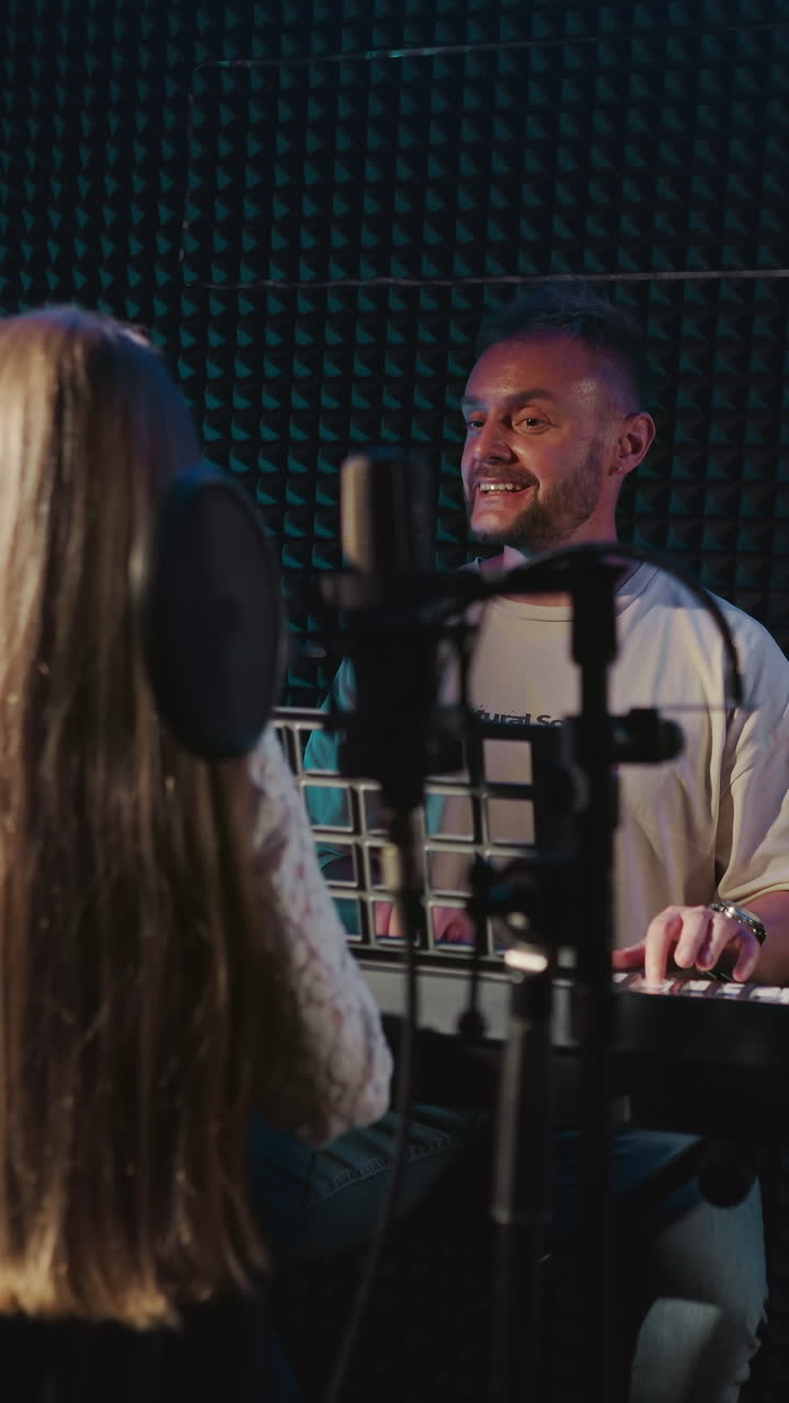 Teacher rehearses song with child in music studio. Smiling father plays piano and looks at little daughter dancing in sound insulated room. Creative family