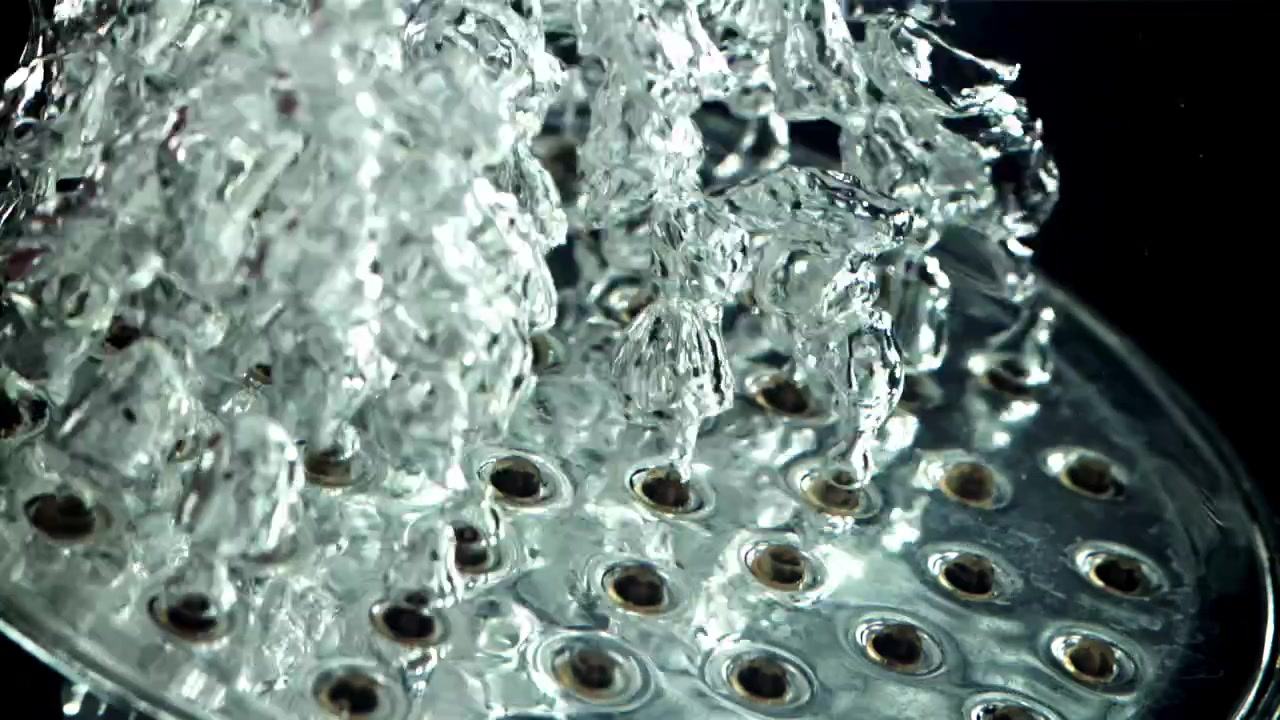 Slow motion close-up van helder water dat uit een douchekop spuit.