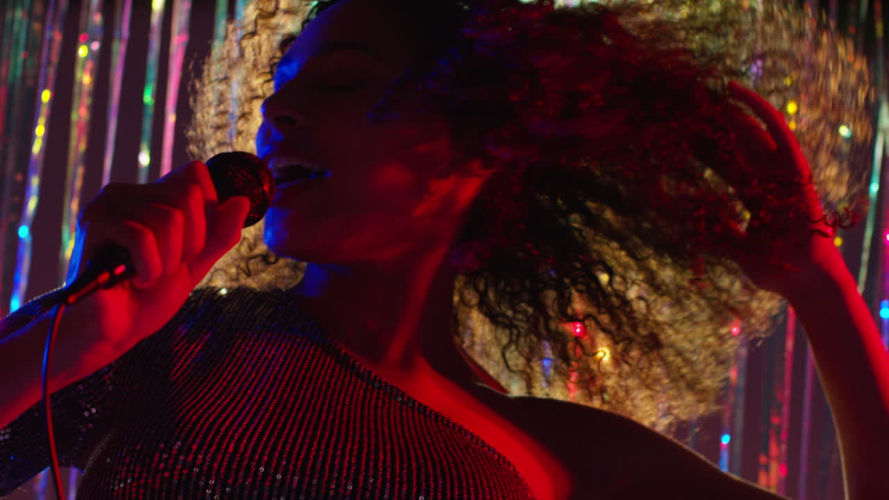Young Woman With Microphone Singing At Karaoke Nightclub Bar Or Disco With Sparkling Lights In Background