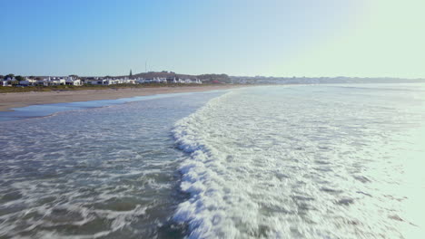 Low drone flight over waves rolling on to long stretch of Paternoster beach