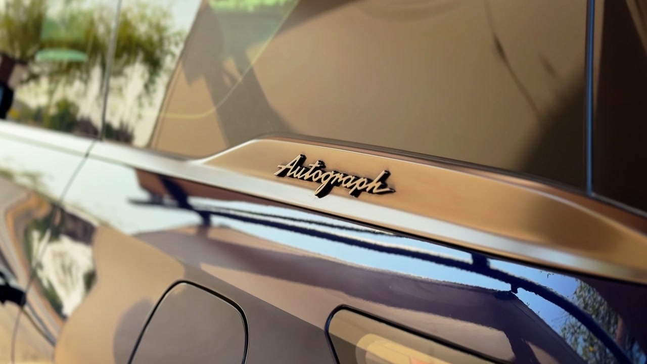 Una toma estática en primer plano del exterior de un SUV de lujo oscuro que presenta el distintivo de acabado específico Autograph. Los árboles y la luz del día se reflejan perfectamente en la pintura brillante y los cristales tintados del vehículo estacionado.