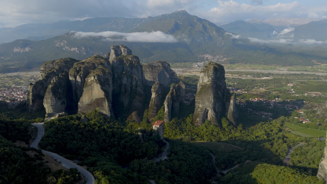 Cinematic aerial view of Meteora monastery in Greece perched on towering cliffs, dramatic rock formations and lush green valley create a breathtaking historic scene