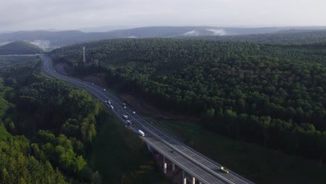 long highway where many vehicles cross it in a forest setting. in weibersbrunn germany, europe. drone aerial 4k footage.