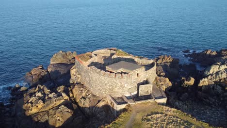 Kurzer-Nahflug-Im-Flug-über-Fort-Doyle-Guernsey-Hinaus-Aufs-Meer-Mit-Zerklüfteter-Küste,-Heideland,-Historischer-Festung-Und-Ausblicken-Bis-Zur-Spitze-Von-Herm-Und-Hinaus-Aufs-Meer-An-Einem-Ruhigen,-Sonnigen-Tag