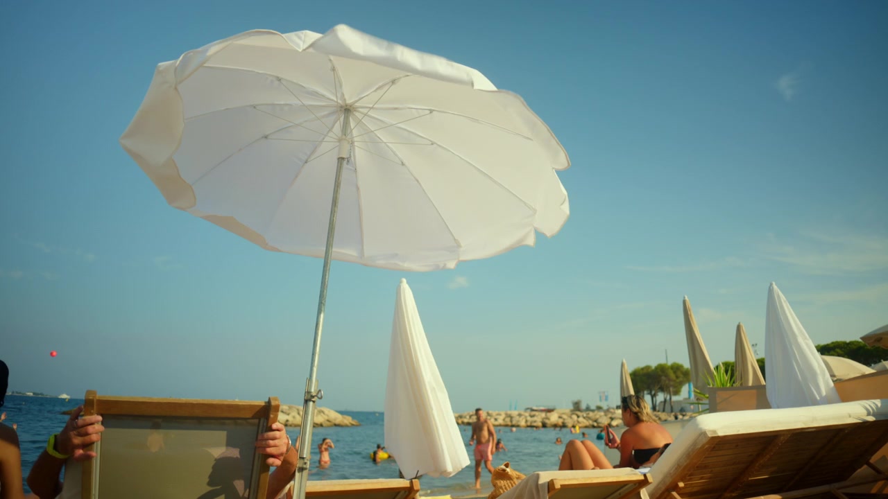 Persone che si godono il tempo libero su una spiaggia sabbiosa sotto un ombrellone bianco, rilassandosi vicino al mare blu.