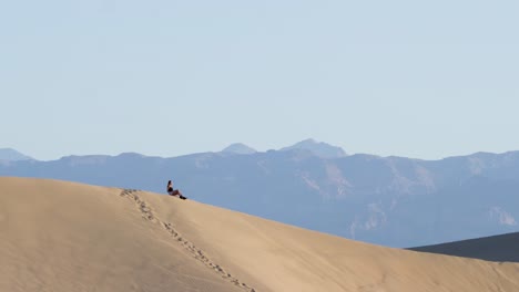 Mujer-Joven-Sentada-En-La-Cima-De-Una-Duna-De-Arena-En-El-Parque-Nacional-Del-Valle-De-La-Muerte-En-California,-Usa---Cámara-Lenta