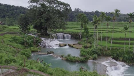 The-Waikelo-Sawah-Waterfall-at-Sumba-with-clear-blue-water-during-a-cloudy-day,-aerial