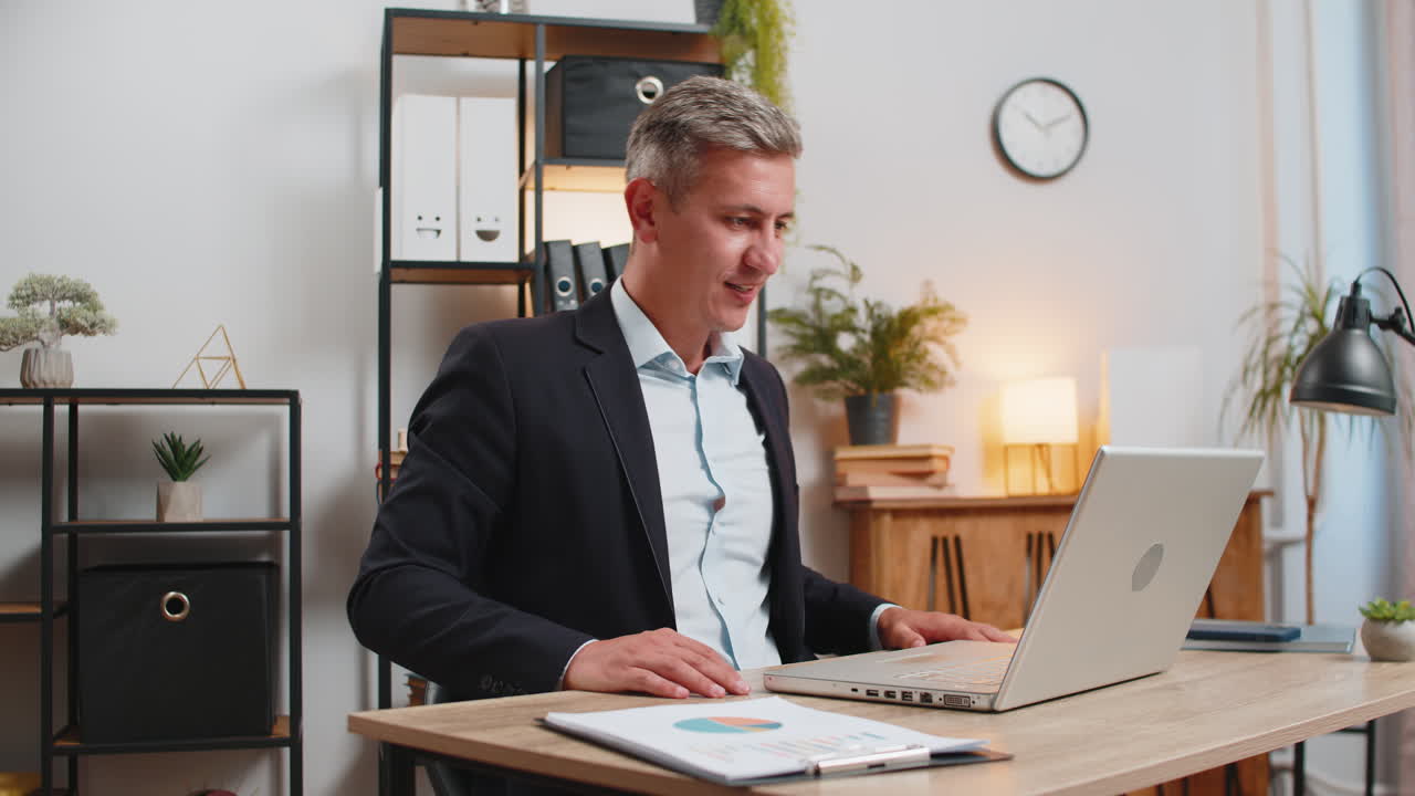 uomo d'affari caucasico fiducioso in abito formale che ha una riunione online con un laptop alla scrivania dell'ufficio di casa